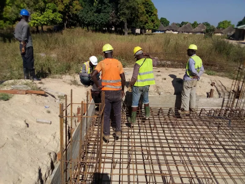 Five professionals wearing hard hats around the steel reinforcement of a building’s foundations.
