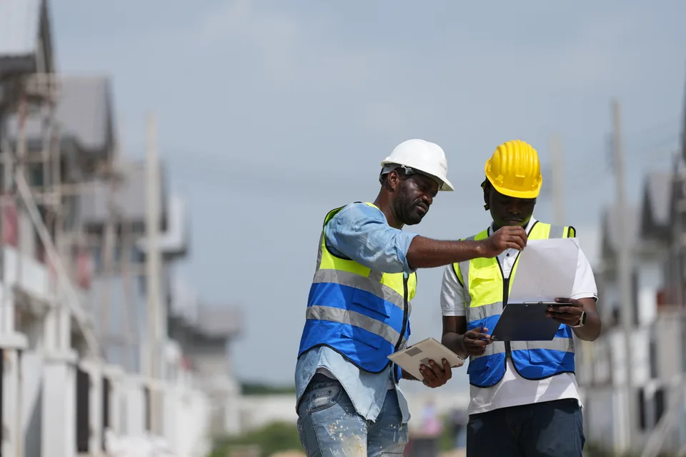 Two professionals wearing hard hats review a document together on a construction site.
