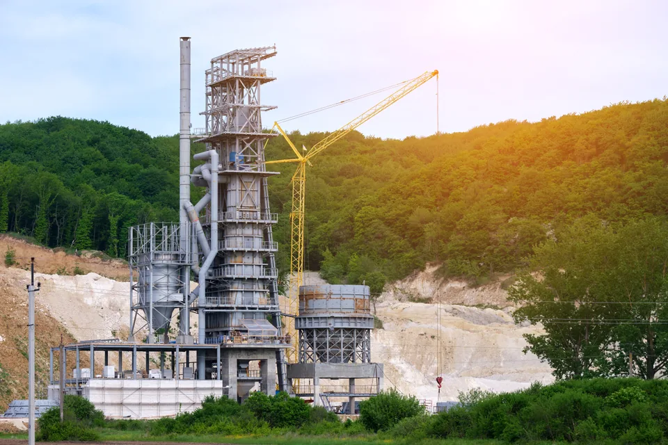 An industrial installation and a crane near a wooded area.